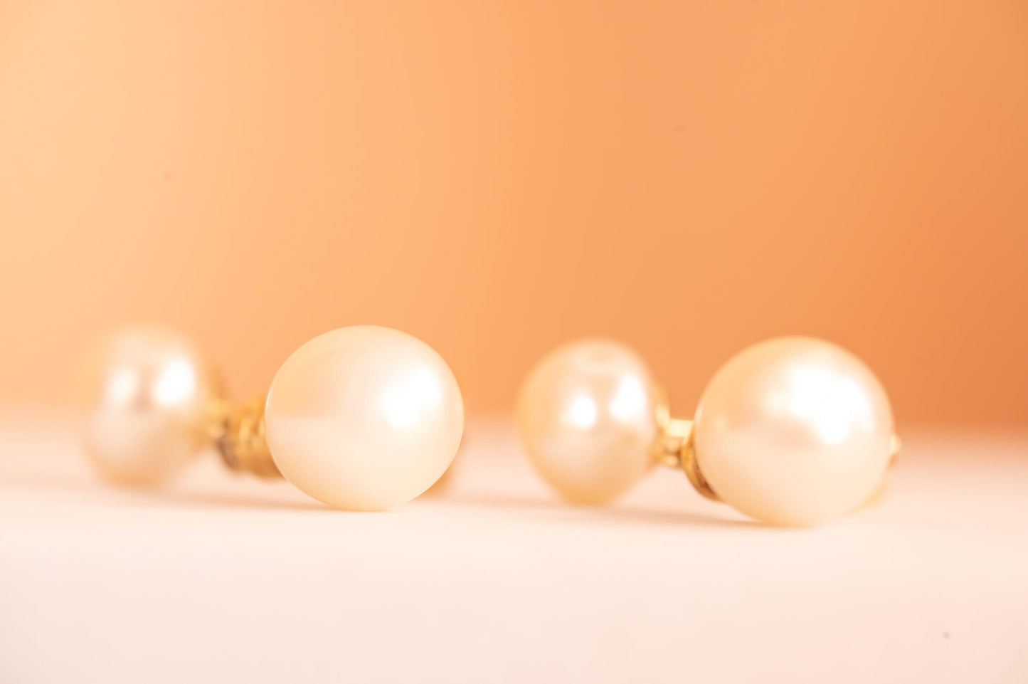 laying flat, side profile of earrings, bright pearls ivory colour on peach background - very romantic