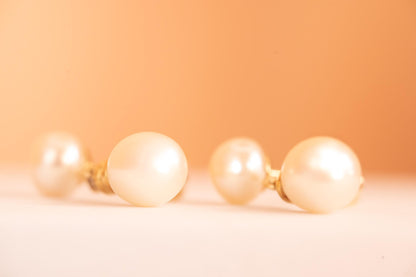 laying flat, side profile of earrings, bright pearls ivory colour on peach background - very romantic